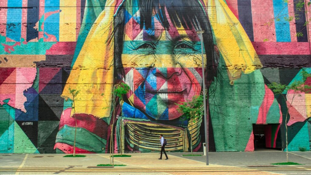 Colorful mural depicting a native face on an urban street wall with a passerby.